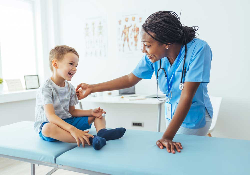Female nurse leans over exam table to check on male child.