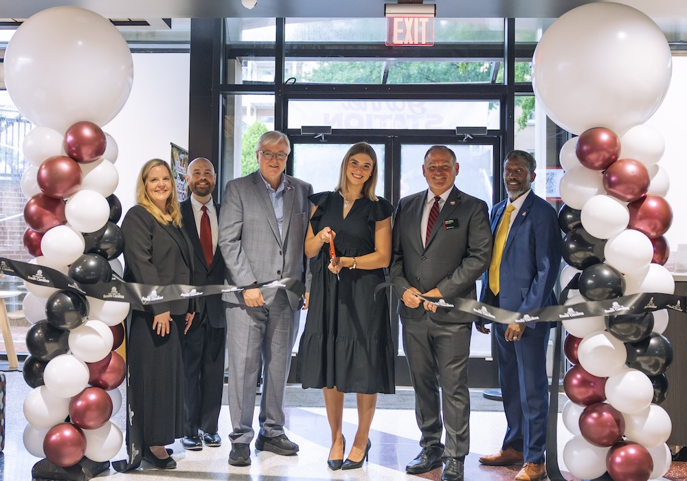 group of people under a garnet and black balloon arch cut a ribbon in a new dining facility