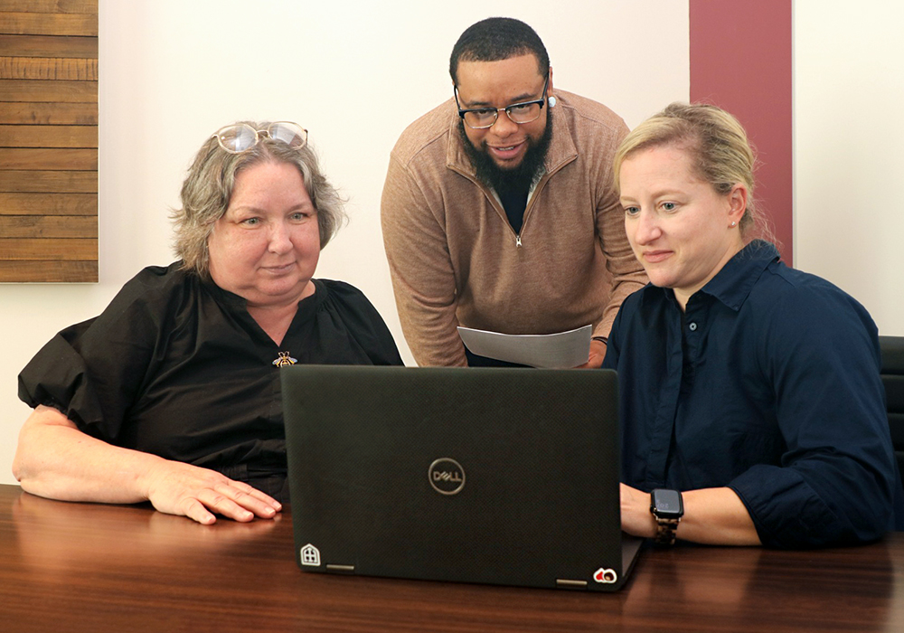 Landon Pitt's looks at a laptop placed on a table, alongside two peers.