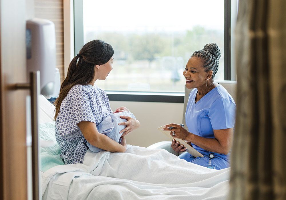 nurse sits at hospital bedside of woman holding infant