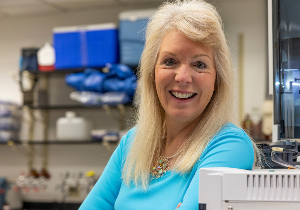 Casual head shot of blonde woman in blue sweater in laboratory setting