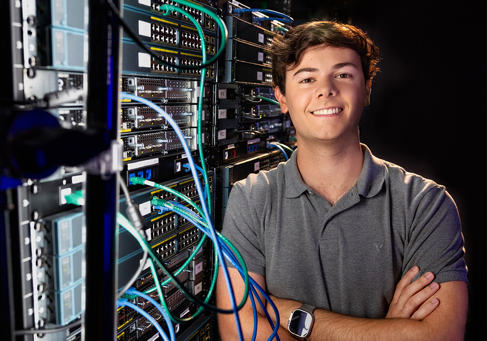 Braden Guliano stands next to a rack of computer equipment