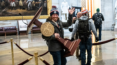 Protestor carrying a podium waving at the camera during the Jan. 6 riot at the U.S. capitol.