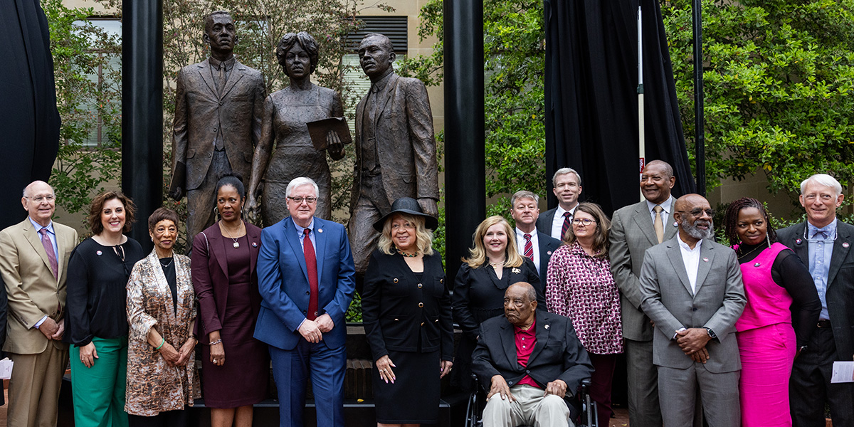 Group photo of the family and university leaders in front of the statue