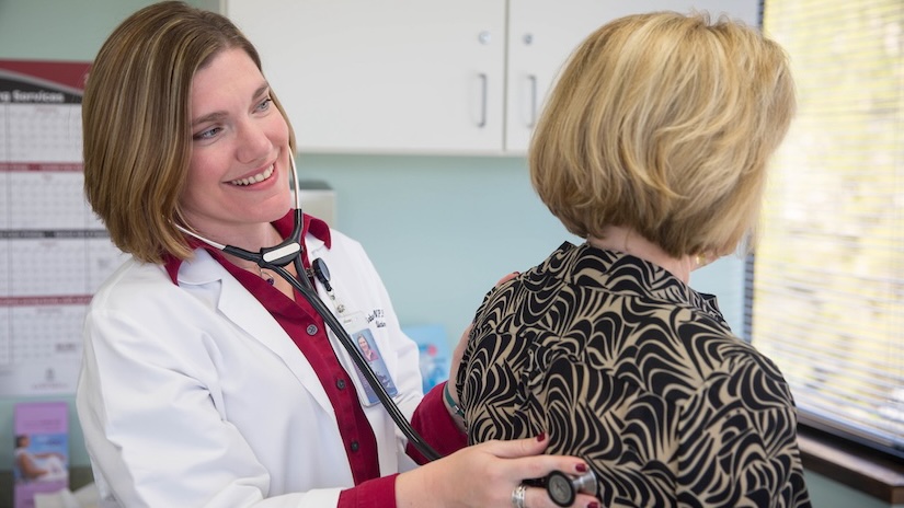 woman in white lab coat examines patient with stethascope