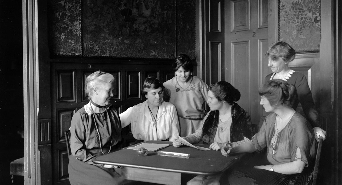     Conferring over ratification [of the 19th Amendment to the U.S. Constitution] at [National Woman's Party] headquarters, Jackson Pl[ace] [Washington, D.C.] 1919. L-R Mrs. Lawrence Lewis, Mrs. Abby Scott Baker, Anita Pollitzer, Alice Paul, Florence Boeckel, Mabel Vernon (standing, right)