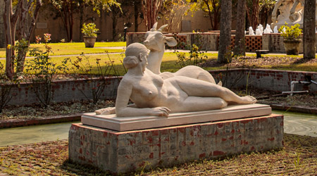 Statue of a woman laying down beside a goat. 