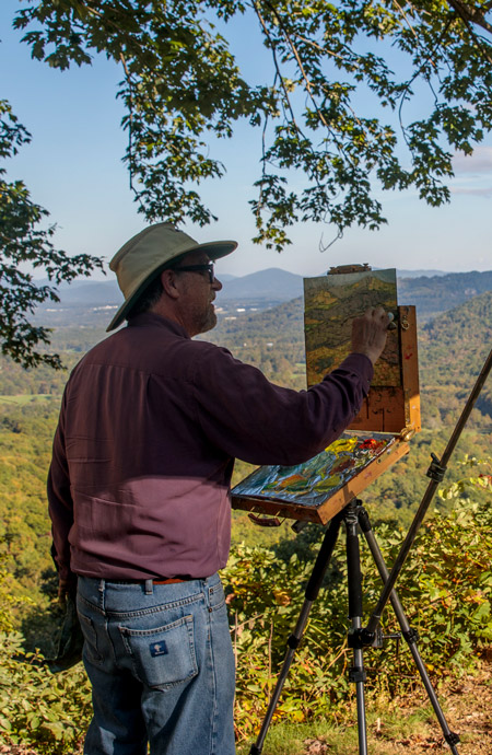 Person painting on an easel overlooking the mountains and hills of the Blue Ridge Parkway. 