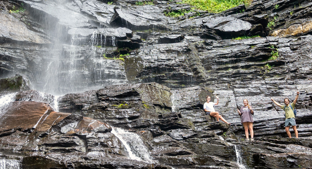 3 students stand along a ledge in a waterfall