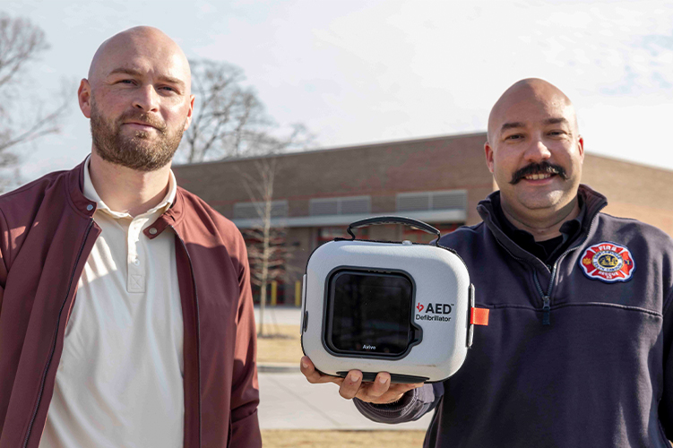 Connor Shaw stands to the left as Caleb Carter shows off an AED like the one that helped save Shaw's life