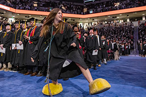 Alumni Sarah Sylvester wearing Cocky's feet while in graduation cap and down at the commencement ceremony. 
