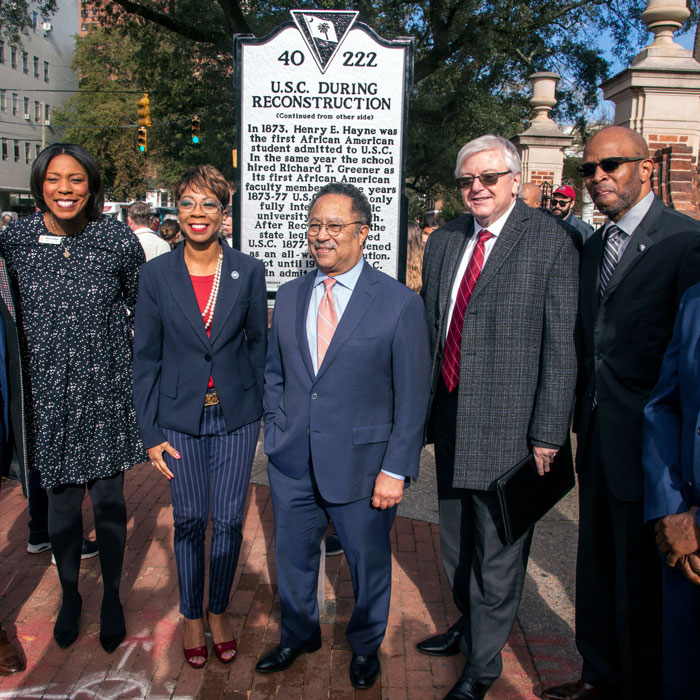 a group of people stand in front of a historical marker commemorating the enrollment of the first Black student at USC during reconstruction