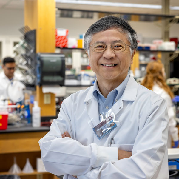 Man in white coat with arms crossed, standing in lab