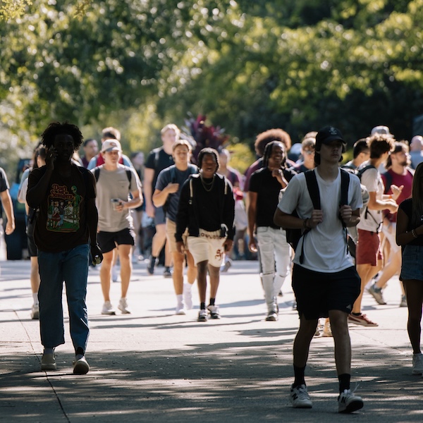 students walking over gray bridge on sunny day