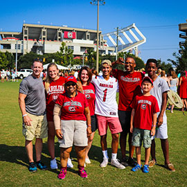 A large Gamecock family smiles at the photographer while standing against the background of Williams-Brice Stadium in the distance