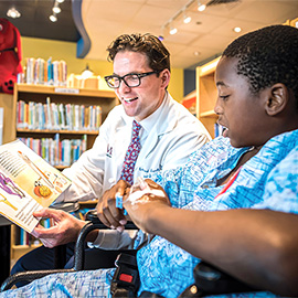Dr. Buchanan and a young boy dressed in a hospital gown reading a book
