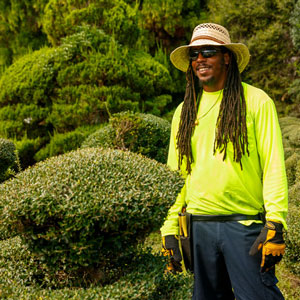 Man in a green shirt and sunglasses standing next to bushes at the Pearl Fryar Topiary Garden