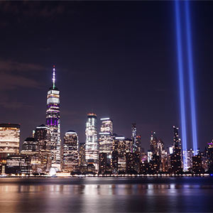 New York City skyline at night with light beams representing the World Trade Center twin towers. 