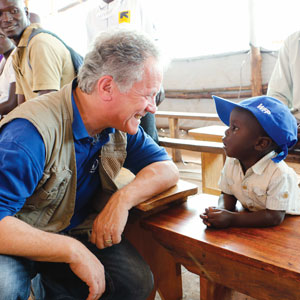 david beasley kneels and smiles at a child in a blue ball cap 