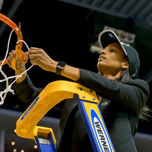 cynthia jordan wearing a ball cap stands on a ladder to cut the net after a big win