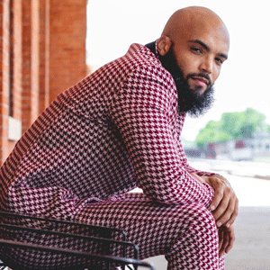 Composer Marcus Norris with shaved head and beard in a maroon houndstooth suit.