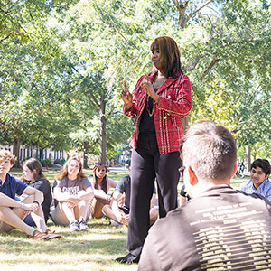 Professor of a U101 class talking to her students sitting in a circle on the Horseshoe. 