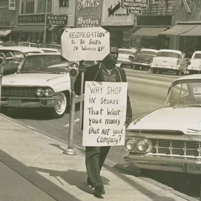 a Black man holds signs protesting segregation
