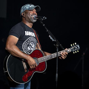 Darius Rucker stands on stage playing the guitar and singing into a microphone