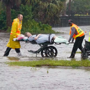 2 health care workers move a woman on a stretcher through floodwaters in Florida