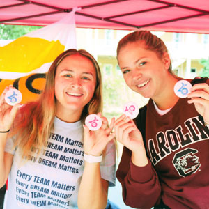 Two female students hold up buttons celebrating the 25 year anniversary of dance marathon.