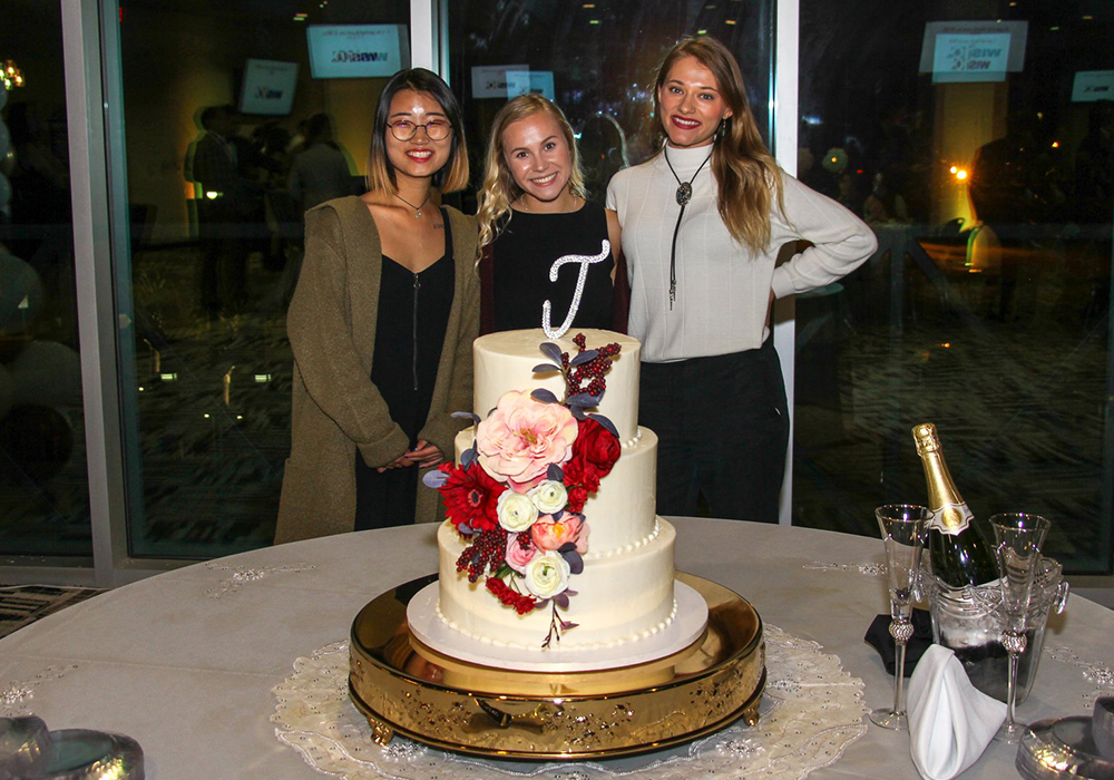three girls standing behind a wedding cake