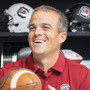 Shane Beamer laughs in his office while handling a football.
