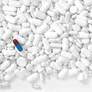 Hundreds of white pills in the background with a single featured blue and red pill