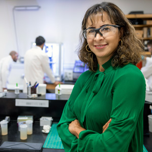 Sanaz Sadati wears safety glass in a lab with workers in lab coats in the background