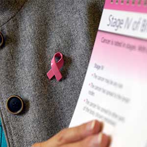 Women wearing a grey sweater and a pink breast cancer awareness pin holds information on stages of breast cancer. 