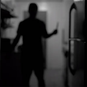 A shadow of a person standing beside a refrigerator holding up a knife in their right hand 