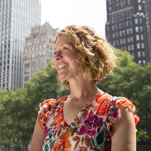 woman stands outside with trees and tall buildings in the background