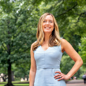 woman stands outdoors with greenery in the background