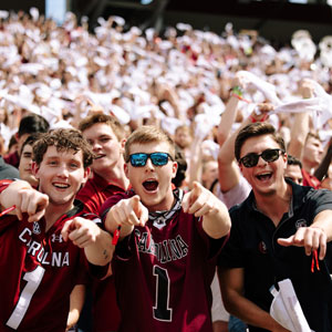 3 young men point at the camera, getting excited at a football game