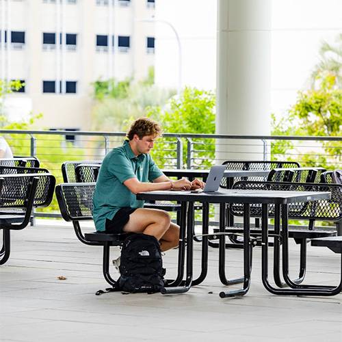 Man sits at a table at Darla Moore studying outside.