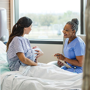 nurse with patient holding infant sitting on bed