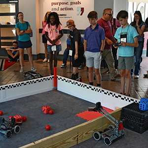 Young students use remotes to control small robots.