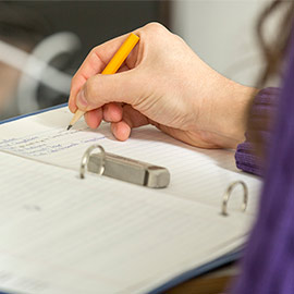 A person holding a pencil and writing in a binder
