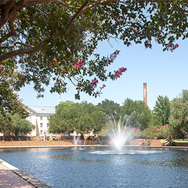 a fountain surrounded by brick walkways with a brick smokestack in the background