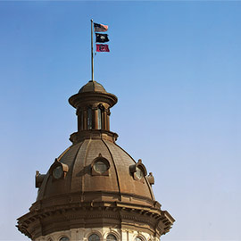 The dome of the South Carolina Statehouse with three flags flying atop, the US, the state and a Gamecock flag