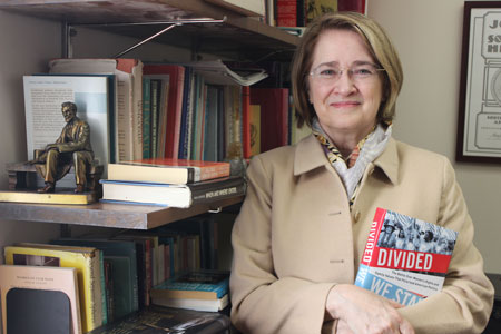Marjorie Spruill stands in front of a book case holding a copy of her book