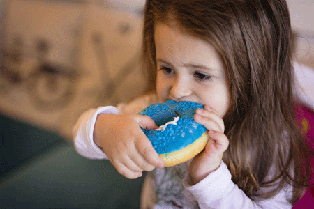 Toddler girl eats a doughnut with blue icing.