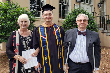 William Brown wearing a cap and gown stands with his parents