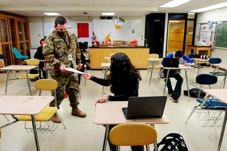 a soldier in uniform hands a paper to a student in a classroom