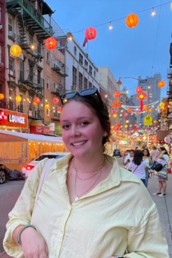 Woman in yellow shirt standing on a city street with orange and red lanterns behind her